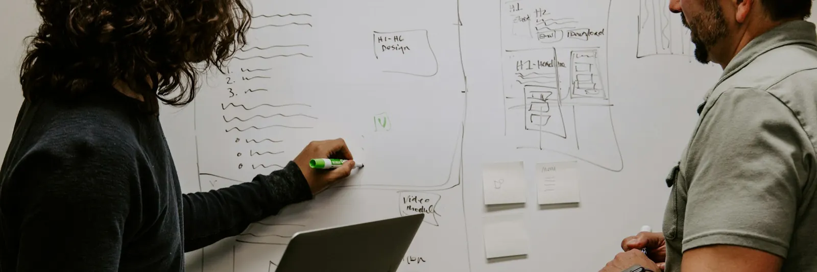 Dos personas bocetando la estructura de una web en una pizarra